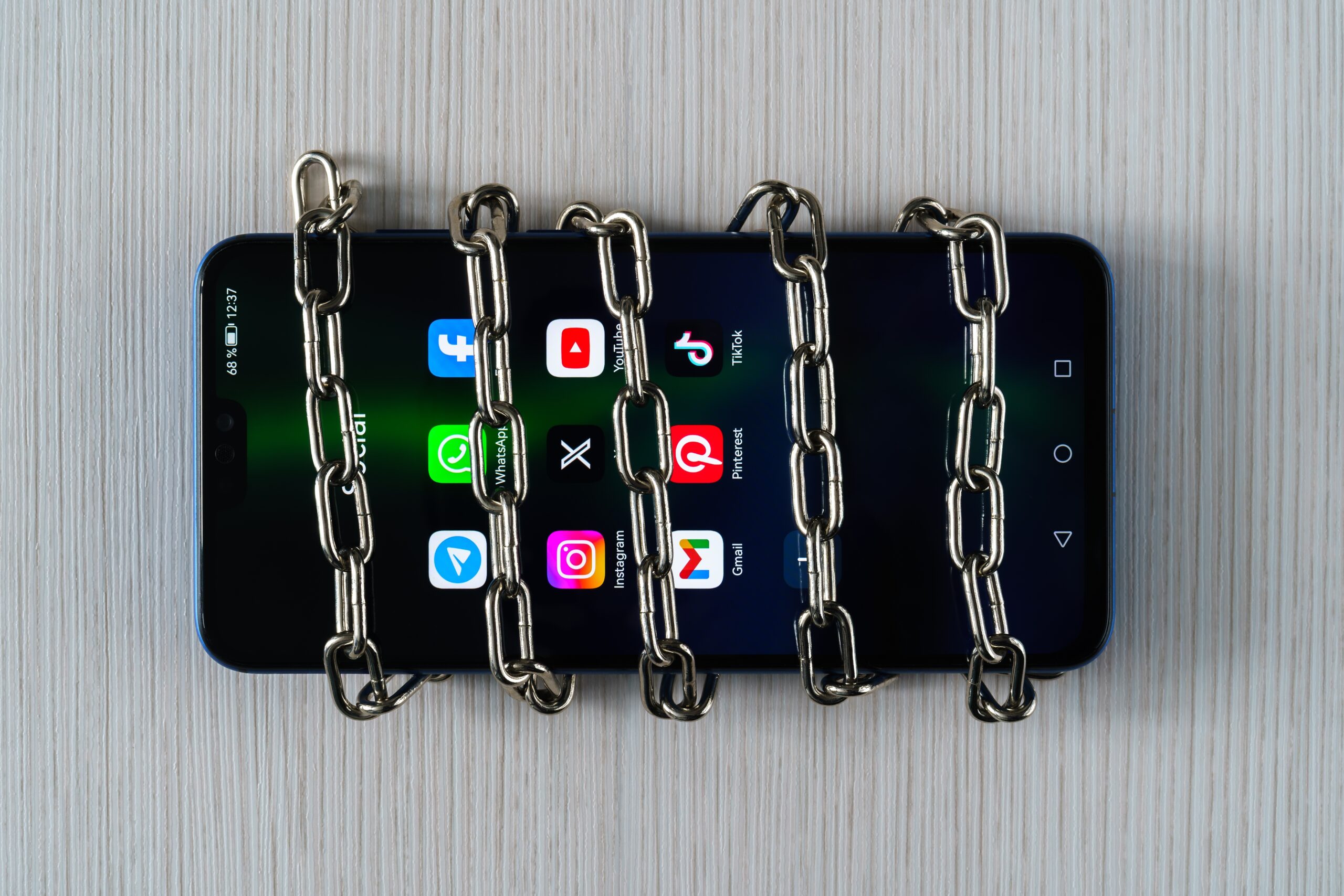 Smartphone wrapped in sturdy metal chains on a light wooden table, conveying a locked or restricted device scenario.