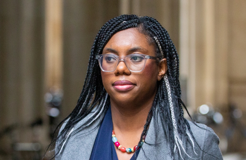 Professional Black woman with braids and clear glasses, wearing a gray blazer and colorful bead necklace, outdoors.